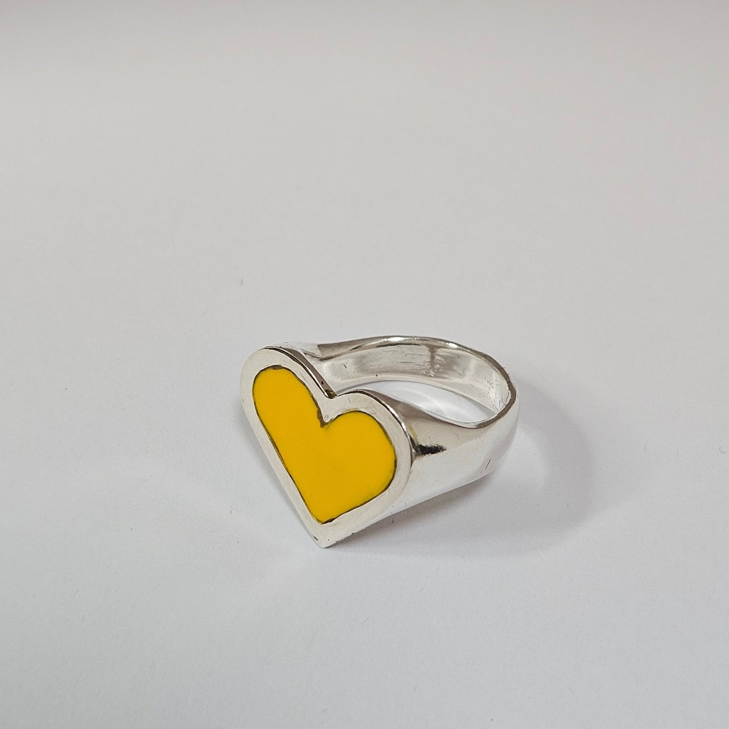 Silver ring with a yellow heart-shaped inset on a light gray background