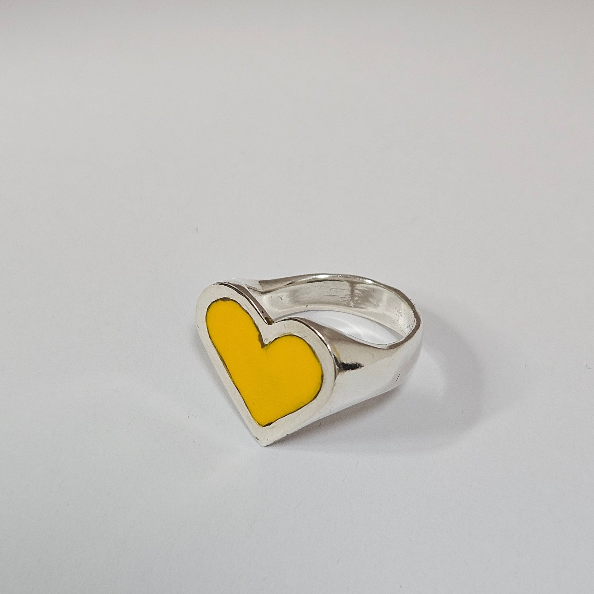 Silver ring with a yellow heart-shaped inset on a light gray background