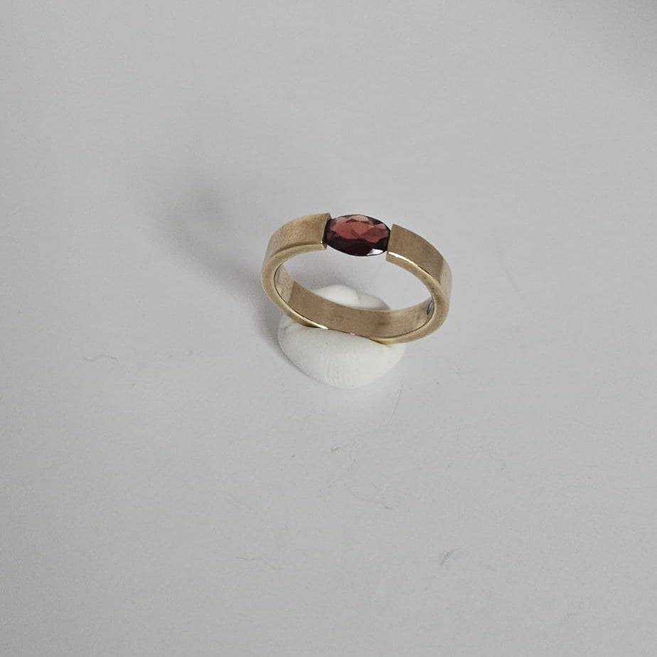 Gold ring with a red gemstone on a light gray background